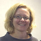 headshot of a smiling woman with rectangular glasses and short, curly, blonde hair. she is wearing a brown top