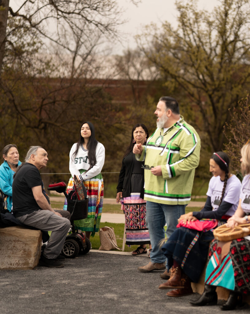 Native man lectures to a group of people outdoors
