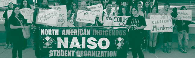 group of students holding posters and banners, the banner in the center reads 'north american indigenous student organization'