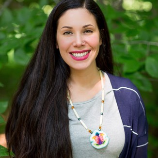 portrait of a smiling woman with long, straight, black hair. she is wearing a gray shirt and striped blue and white cardigan with a shell necklace